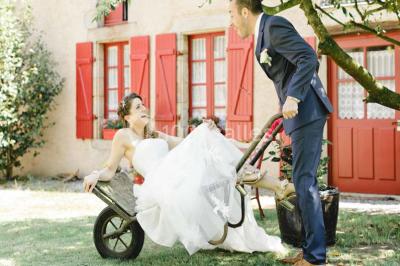 Une mariée en robe blanche est assise sur un banc en bois décoré des lettres ’A&J’, tenant un bouquet de fleurs.