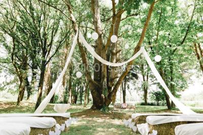 Une mariée en robe blanche est assise sur un banc en bois décoré des lettres ’A&J’, tenant un bouquet de fleurs.