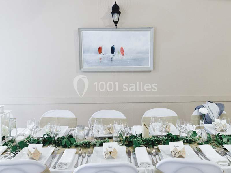 Table élégamment dressée avec vaisselle blanche, décoration végétale et tableau encadré représentant des voiliers au mur.