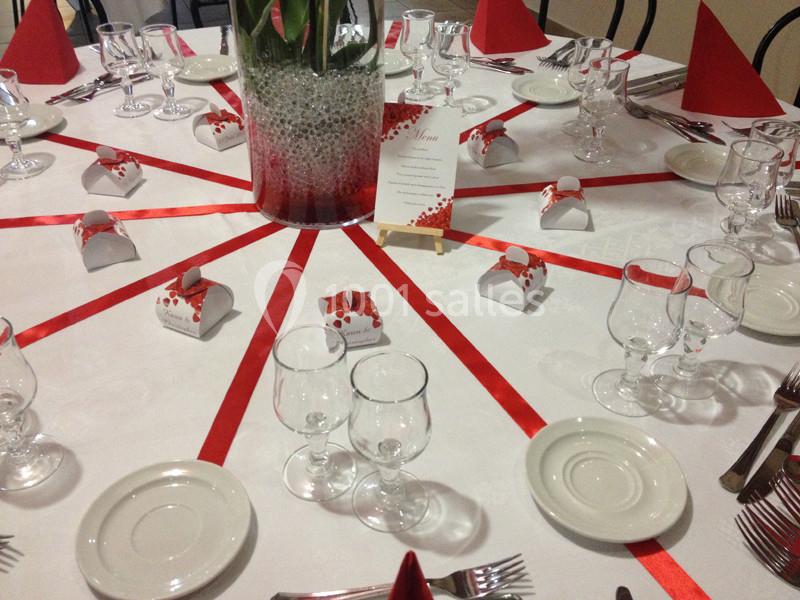 Table décorée pour un événement avec rubans rouges, verres, assiettes, couverts et boîtes cadeaux blanches.
