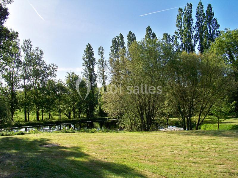 Vue d'un étang entouré d'arbres et d'une pelouse sous un ciel bleu dégagé.