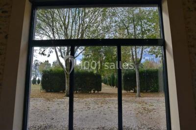 Vue aérienne d'un jardin arboré avec des allées herbeuses, entouré de champs et de quelques bâtiments résidentiels.