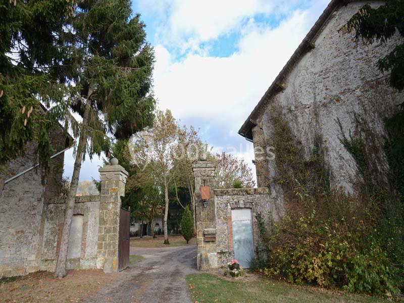 Entrée d'une propriété avec portail en pierre, entourée de bâtiments anciens et de végétation automnale.