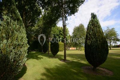 Vue aérienne d'un jardin arboré avec des allées herbeuses, entouré de champs et de quelques bâtiments résidentiels.
