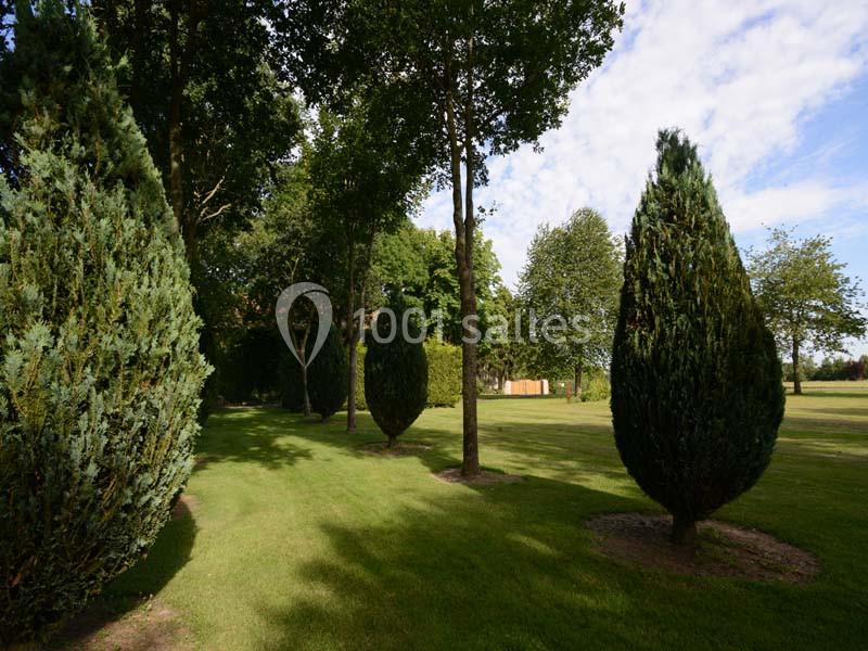 Alignement d'arbres et d'arbustes taillés sur une pelouse verte, sous un ciel partiellement nuageux.