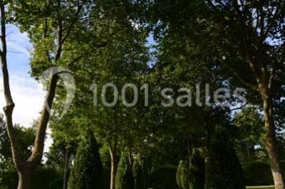 Vue aérienne d'un jardin arboré avec des allées herbeuses, entouré de champs et de quelques bâtiments résidentiels.