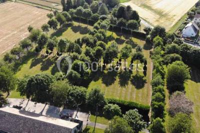 Vue aérienne d'un jardin arboré avec des allées herbeuses, entouré de champs et de quelques bâtiments résidentiels.