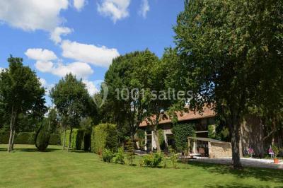 Vue aérienne d'un jardin arboré avec des allées herbeuses, entouré de champs et de quelques bâtiments résidentiels.