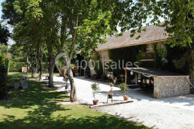 Vue aérienne d'un jardin arboré avec des allées herbeuses, entouré de champs et de quelques bâtiments résidentiels.