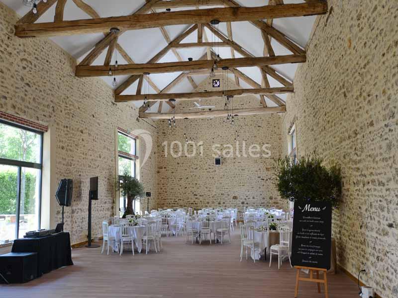 Salle de réception lumineuse avec murs en pierre, poutres apparentes, tables dressées et grandes fenêtres donnant sur l…