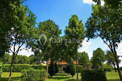 Vue aérienne d'un jardin arboré avec des allées herbeuses, entouré de champs et de quelques bâtiments résidentiels.