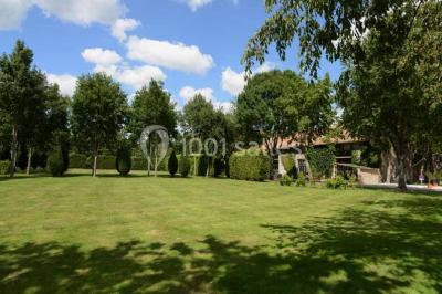 Vue aérienne d'un jardin arboré avec des allées herbeuses, entouré de champs et de quelques bâtiments résidentiels.