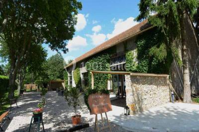 Vue aérienne d'un jardin arboré avec des allées herbeuses, entouré de champs et de quelques bâtiments résidentiels.