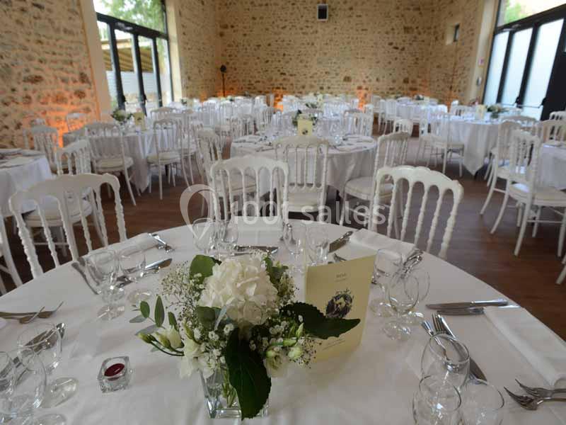 Salle de réception décorée avec des tables rondes dressées, nappes blanches et compositions florales.