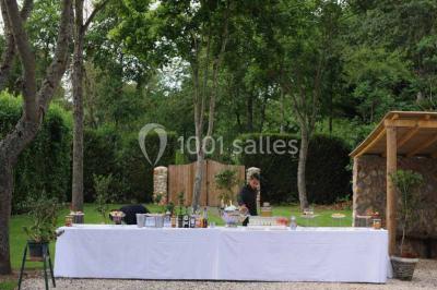 Vue aérienne d'un jardin arboré avec des allées herbeuses, entouré de champs et de quelques bâtiments résidentiels.