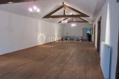 Salle lumineuse avec grandes fenêtres, mobilier en rotin gris et poutres apparentes, donnant sur un espace extérieur…