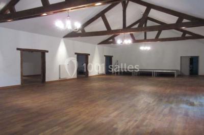 Salle lumineuse avec grandes fenêtres, mobilier en rotin gris et poutres apparentes, donnant sur un espace extérieur…