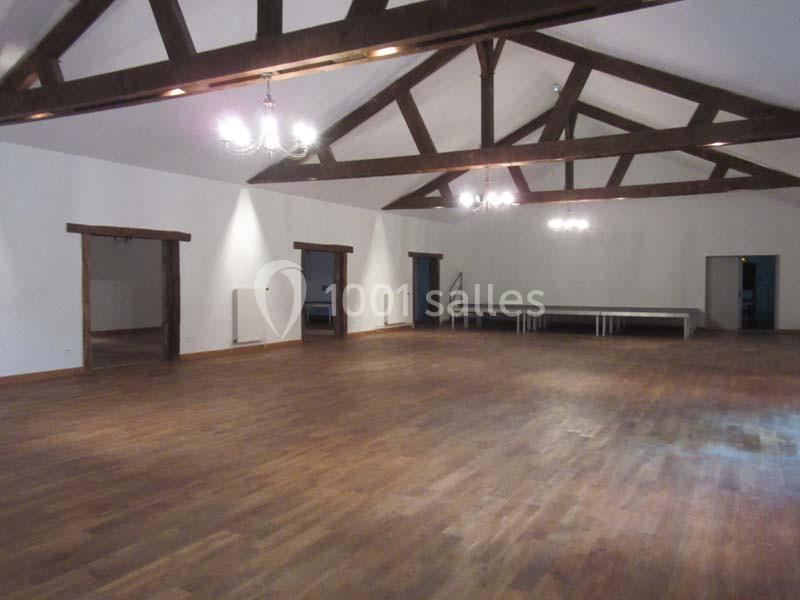 Salle spacieuse avec parquet en bois, poutres apparentes au plafond et éclairage par des lustres suspendus.