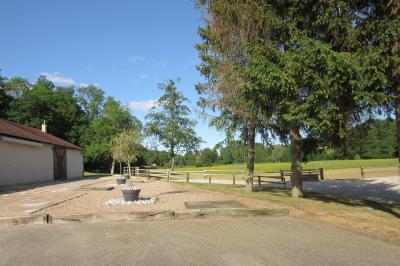 Salle lumineuse avec grandes fenêtres, mobilier en rotin gris et poutres apparentes, donnant sur un espace extérieur…