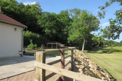 Salle lumineuse avec grandes fenêtres, mobilier en rotin gris et poutres apparentes, donnant sur un espace extérieur…
