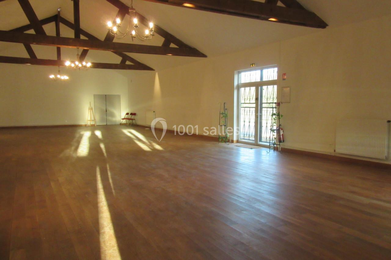 Salle spacieuse avec parquet en bois, poutres apparentes, grandes fenêtres et lumière naturelle entrant.