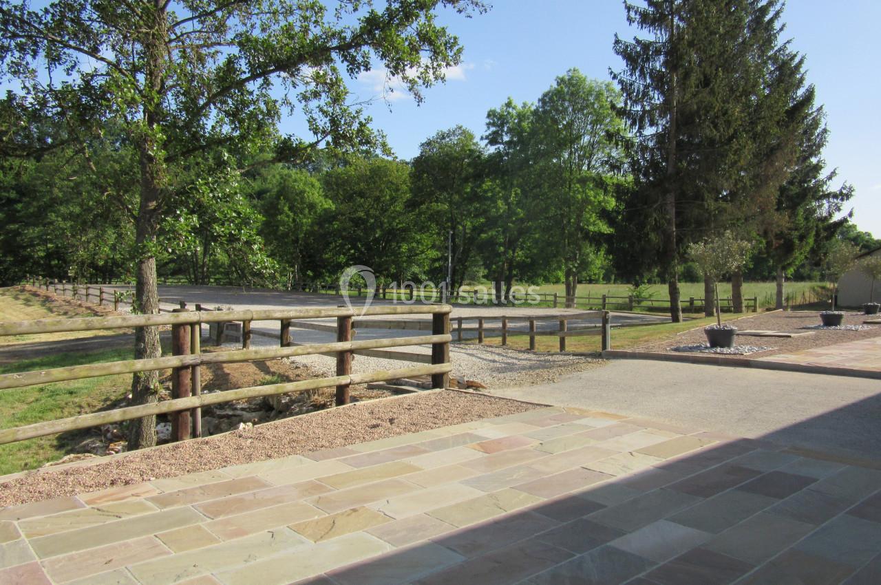 Allée bordée de clôtures en bois, entourée d'arbres et de pelouses, avec un sol en pierre au premier plan.