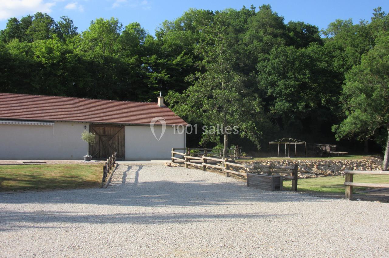 Cour gravillonnée avec une grange à toit rouge, clôtures en bois et arbres en arrière-plan.