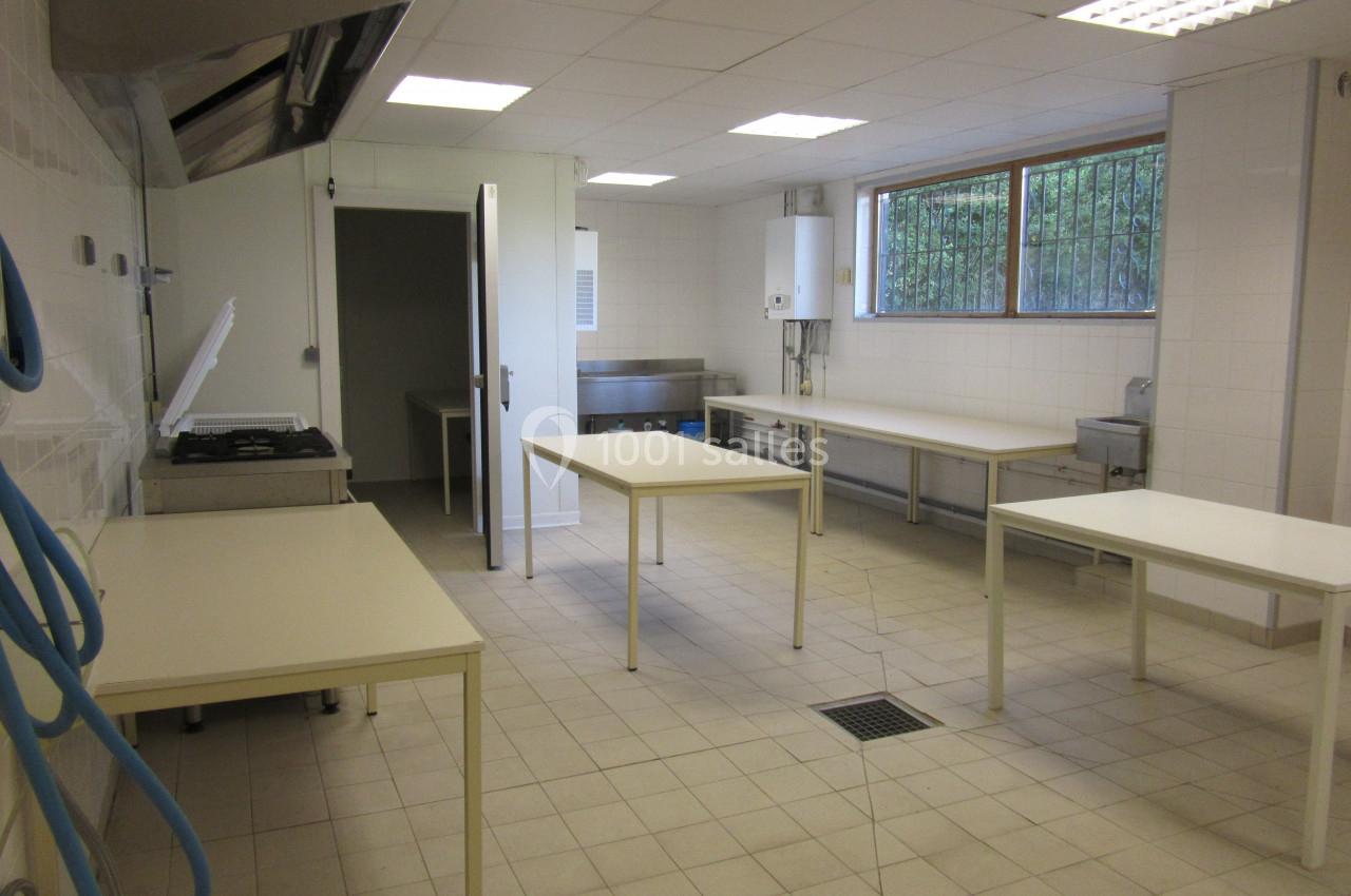 Cuisine professionnelle vide avec plans de travail, évier, hotte d'extraction et carrelage blanc au sol et aux murs.