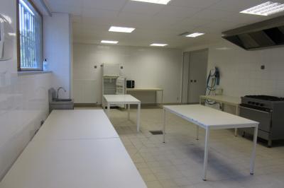 Salle lumineuse avec grandes fenêtres, mobilier en rotin gris et poutres apparentes, donnant sur un espace extérieur…