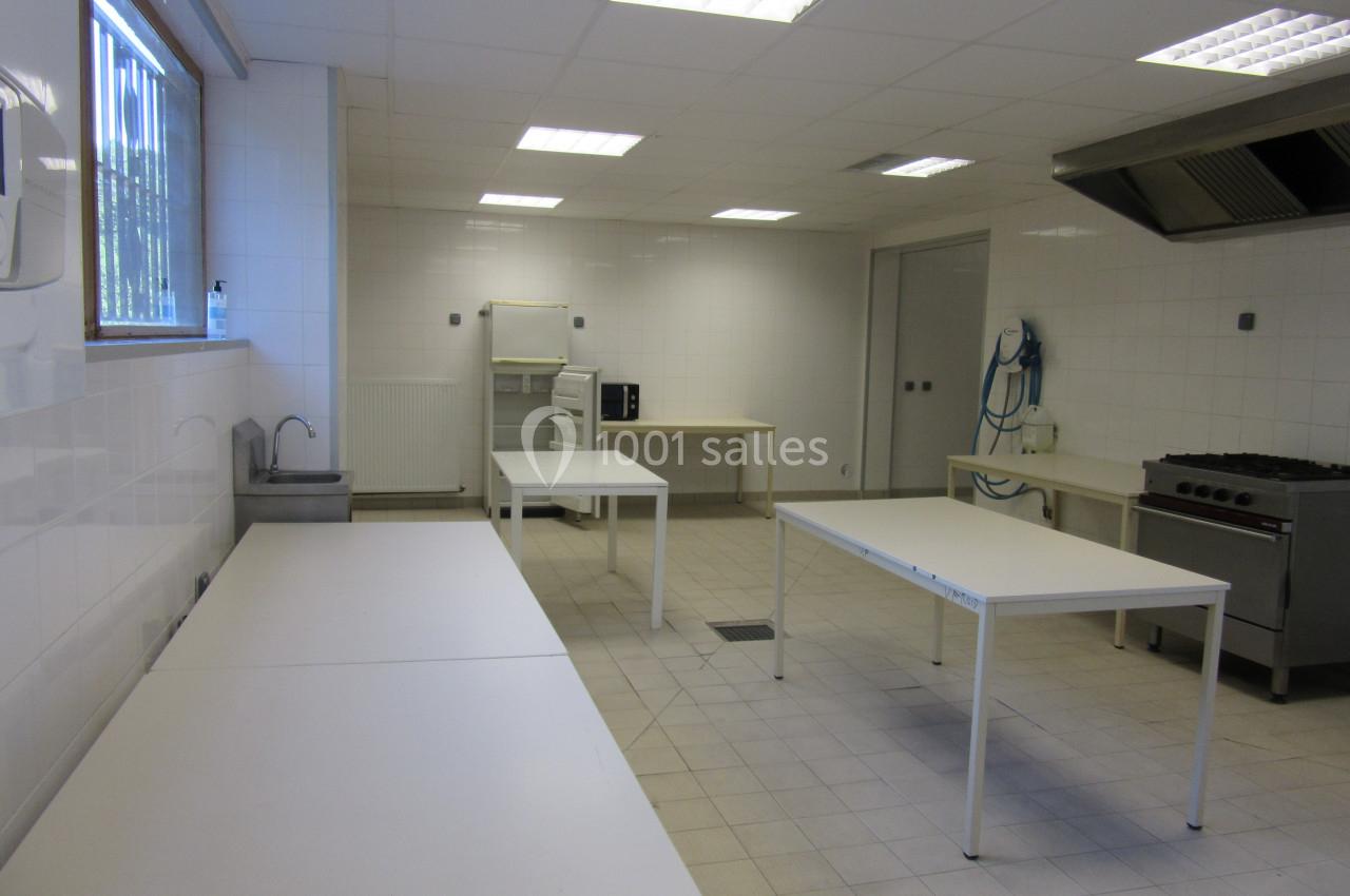 Cuisine professionnelle vide avec plans de travail blancs, évier, hotte, four et carrelage clair.