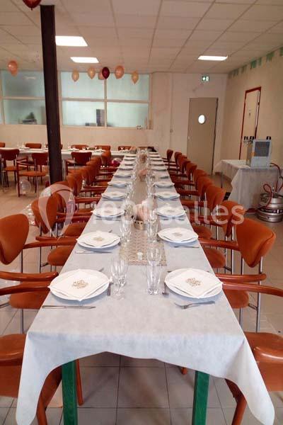 Salle aménagée avec une longue table dressée pour un repas, comprenant assiettes, verres et serviettes blanches.