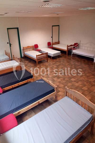 Salle avec plusieurs lits simples alignés, matelas visibles, sol en carrelage et murs clairs.