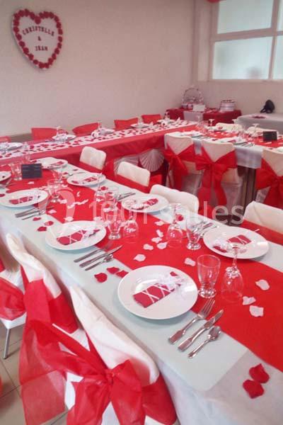 Tables décorées en rouge et blanc avec nappes, rubans et pétales, préparées pour un événement festif ou un repas.