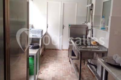 Évier double en inox avec robinet flexible, lave-vaisselle professionnel et sol en carrelage beige dans une cuisine.