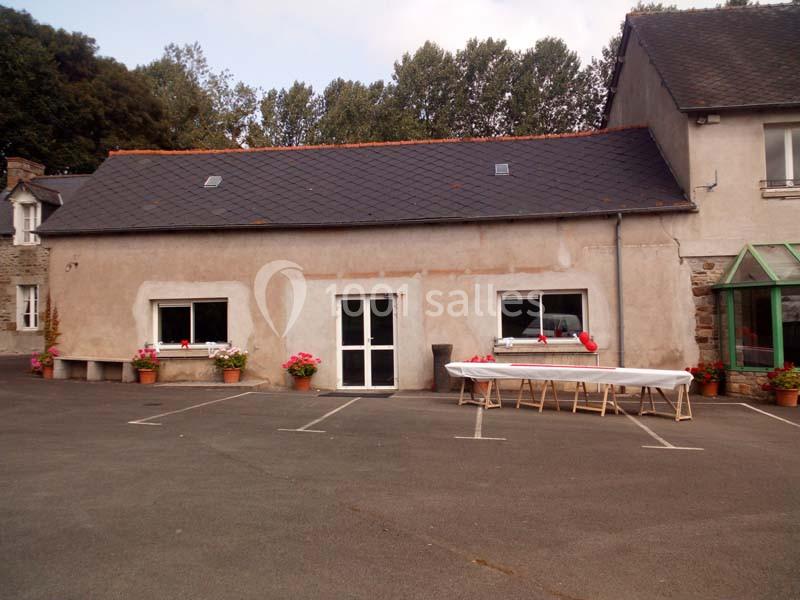 Façade d'un bâtiment avec toit en ardoise, deux fenêtres, une porte centrale et une table dressée à l'extérieur.