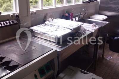 Évier double en inox avec robinet flexible, lave-vaisselle professionnel et sol en carrelage beige dans une cuisine.