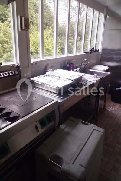 Cuisine professionnelle avec plan de travail en inox, équipements de cuisson, fenêtres lumineuses et vue sur l'extérieur.