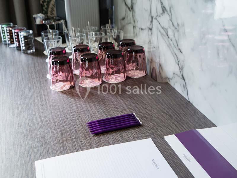 Verres violets, crayons et feuilles de papier disposés sur une table en bois devant un mur en marbre.