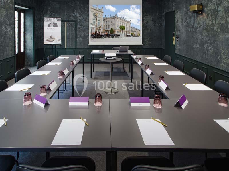 Salle de réunion aménagée avec tables en U, chaises, blocs-notes, stylos et écran de projection en arrière-plan.