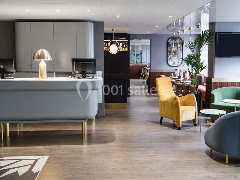 Espace d'accueil moderne avec comptoir, fauteuils colorés, plantes et éclairage chaleureux.