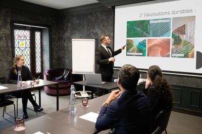 Une femme présente des informations sur un écran à trois personnes assises dans une salle de réunion décorée.