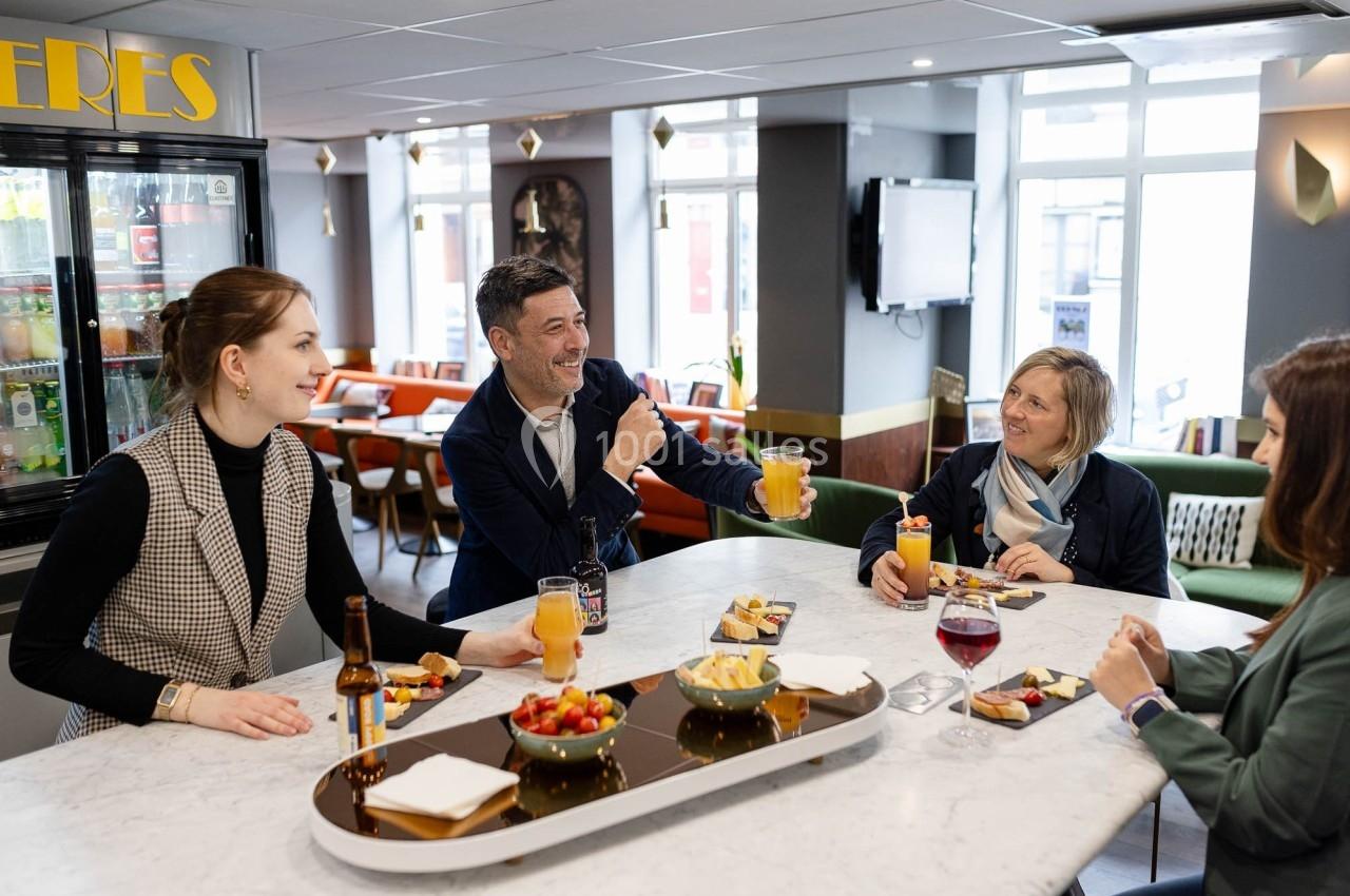 Quatre personnes discutent autour d'une table dans un café, avec des boissons et des collations.