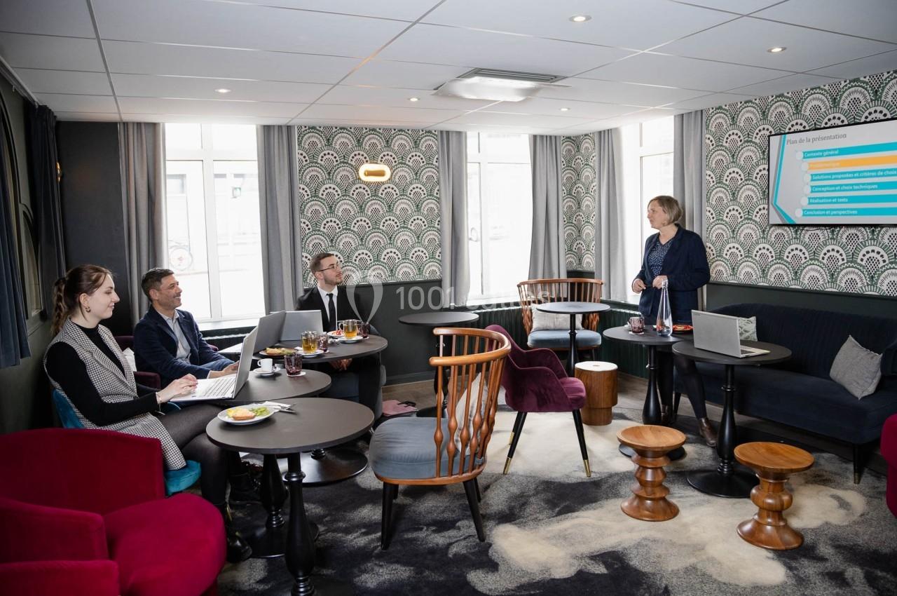 Une femme présente des informations sur un écran à trois personnes assises dans une salle de réunion décorée.