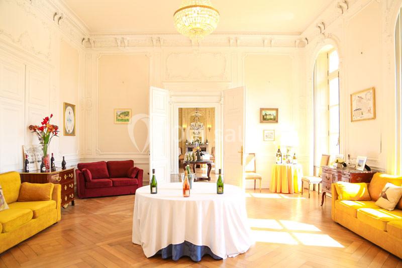 Salon lumineux avec parquet, mobilier classique, table ronde dressée au centre et lustre en cristal au plafond.