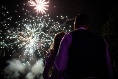 Un couple regarde un feu d'artifice illuminant le ciel nocturne avec des éclats de lumière colorés.