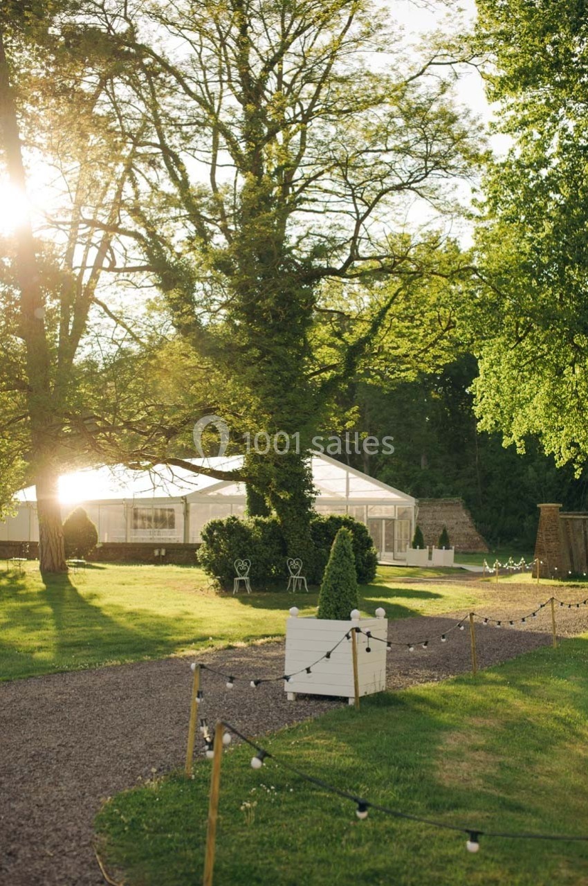 Un grand arbre au centre d'un jardin verdoyant avec une tente transparente en arrière-plan sous une lumière douce.