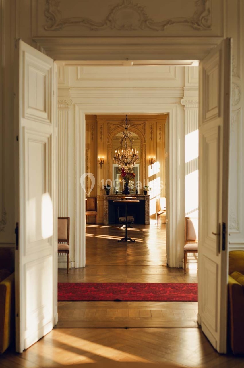 Vue d'un intérieur élégant avec des portes ouvertes, un lustre, une cheminée et un tapis rouge éclairés par la lumière…