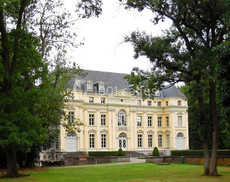 Façade d'un château jaune à trois étages entouré d'arbres et situé dans un parc verdoyant.