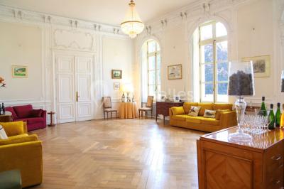 Salon lumineux avec parquet, mobilier classique, table ronde dressée au centre et lustre en cristal au plafond.