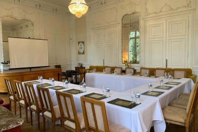 Salon lumineux avec parquet, mobilier classique, table ronde dressée au centre et lustre en cristal au plafond.